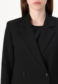 Černý upravený blazer s klopami a zapínáním na dvojité knoflíky. Vyroben z hladké látky, má strukturované ramena a čistý design.