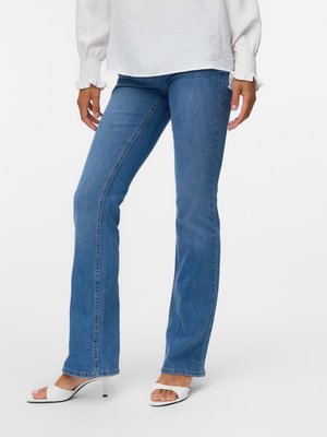 Fitted blue denim flared jeans with slight fading, paired with a textured white blouse and open-toe white heeled sandals.
