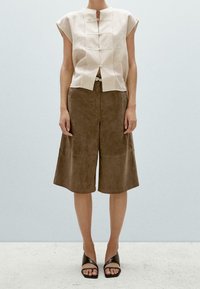 Beżowy lniany top z krótkimi rękawami typu cap, z detalami guzików z przodu. Brązowe zamszowe kuloty o szerokim kroju nogawek. Czarne sandały na paski.