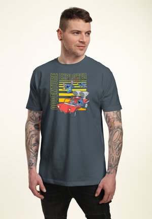 Mand med tatoveringer iført mørkeblå t-shirt med animerede figurer, der kører en rød dune buggy med teksten "Adventure Explorer".