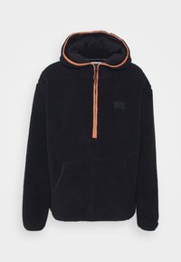 Felpa nera in pile con accenti arancioni, con zip a metà davanti, grande tasca frontale e una finitura testurizzata e accogliente. Presenta un cappuccio con una fodera in contrasto.