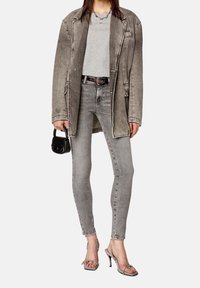 Přesahující šedá denimová bunda přes šedé tričko, v kombinaci se šedými úzkými džíny a metalickými sandály na podpatku, doplněná malou černou kabelkou.