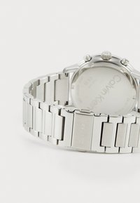 Montre en acier inoxydable argenté avec un bracelet lisse et poli composé de maillons rectangulaires, et un boîtier rond avec des éléments matériels visibles.