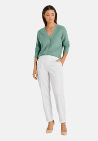 Mintgroene cardigan met V-hals en knoopsluiting, gecombineerd met witte tapered broek en beige hoge hakken. Gladde textuur, casual pasvorm.