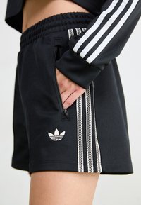 Svarte treningsshorts med snor i livet, med tre hvite striper på sidene og en liten hvit logo på kanten.