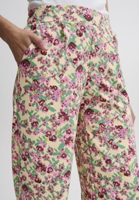 Pantalons à motifs floraux crème, ornés de fleurs violettes et vertes. Comprend des poches latérales et une texture de tissu lisse.