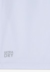 Tissu blanc évacuant l'humidité avec un motif texturé en forme de losange. Présente le logo "ULTRA DRY" en gris près du bord inférieur.