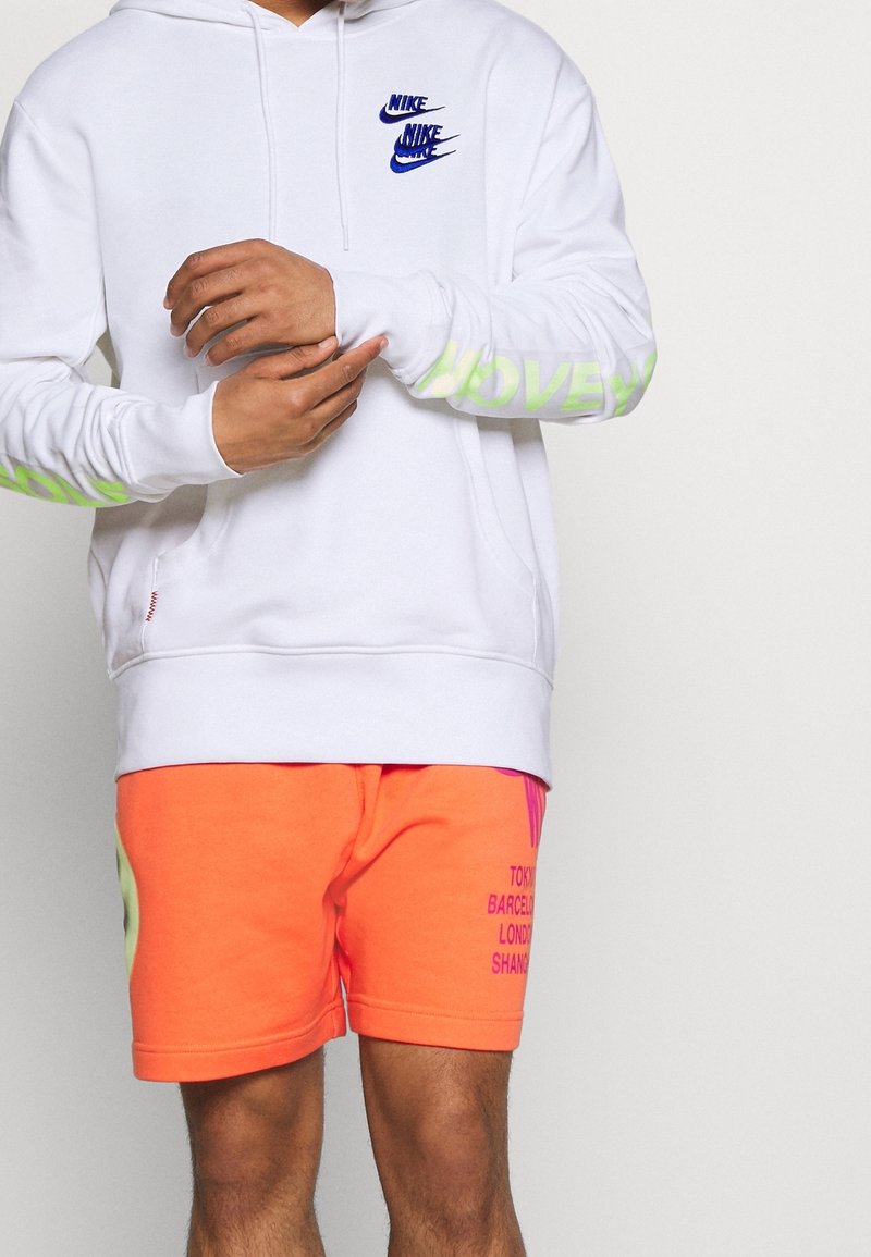 Vit hoodie med blå Nike-logotyper och grön "LOVE"-text på ärmarna, kombinerad med lysande orange shorts med stadsnamn i lila tryck.