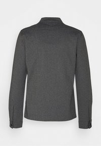 Chemise à manches longues gris foncé avec poignets boutonnés vue de dos sur un fond gris clair uni.
