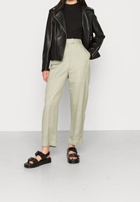 Czarna skórzana kurtka motocyklowa, dopasowany czarny top z ryflem, jasnoszare spodnie w szerokim kroju i masywne czarne sandały z dużymi klamrami.