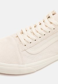 Baskets en daim beige avec surface texturée, présentant une bande logo, des lacets ronds, et une semelle en caoutchouc. Accents en écru.