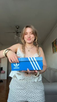 Blue Adidas shoebox with three white stripes on the side, held in a person's hands, featuring a flat lid and smooth, glossy texture.