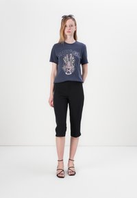 T-shirt grafico blu navy con stampa di un tigre, abbinato a pantaloni capri neri aderenti. Sandali neri con cinghie completano l'outfit.