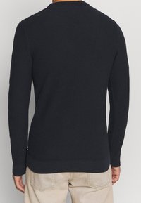 Mörk marinblå texturerad tröja med långa ärmar, rundad halsringning och ribbad nederkant. Har subtila sidodetaljer och en figursydd siluett.