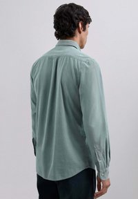 Lys grønt langærmet skjorte med knapmanschetter, blød tekstur, lige kant og rygklapdetalje. Stoffet ser lidt krøllet ud.