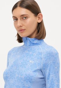 Ανοιχτό μπλε φούτερ με φερμουάρ και γεωμετρικό σχέδιο, ριγωτή υφή στα μανίκια και μικρό λευκό λογότυπο στο στήθος.