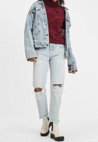 Lichtblauwe ripped jeans met rafelige hemmen, gecombineerd met een bordeauxrode trui en een vervaagde spijkerjack. Crème-kleurige platformbotten maken de look compleet.