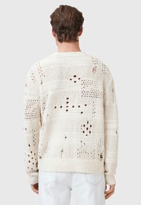 Chunky knit sweater in off-white with openwork patterns, textured surface, and irregular holes. Ribbed cuffs and hem detail.