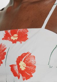 Vestido com padrão floral apresentando uma base de tecido branca com papoulas vermelhas intensas, caules verdes e finas alças nos ombros. Textura suave e design ajustado.
