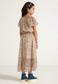 Luipaardprint jurk met korte fladdermouwen, elastische taille en gelaagde rok. Gepaarde met blauwe hoge sneakers en een bijpassende haarband.
