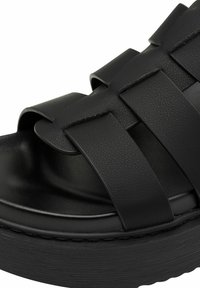 Black platform sandals with wide, woven straps made of textured material, featuring a curved footbed and a thick, ridged sole.