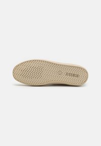 Suola di sneaker beige con motivo di battistrada a zigzag, texture liscia e fori di ventilazione. Marchio visibile sul tallone.