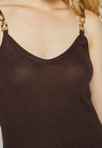 Brun ribbet tanktop med V-halsudskæring, udstyret med guld kædetræk og en subtil glimmer tekstur.