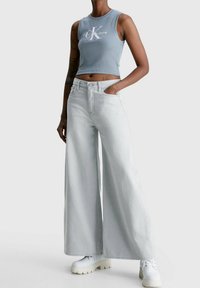 Un crop top bleu clair à côtes avec un logo blanc, associé à un jean large délavé et des baskets blanches à plateforme.