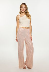 Beige top met één schouderband, gecombineerd met brede roze paillettenbroek met een diamanten patroon en een gladde textuur.