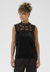 Top senza maniche nero con yoke in pizzo, scollatura a onda e corpo in morbido velluto. Presenta dettagli in pizzo floreale intricati.