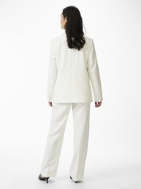 Costum alb, croit, format dintr-un blazer structurat și pantaloni largi. Material neted, cu un design curat, completat de tocuri ajustate.