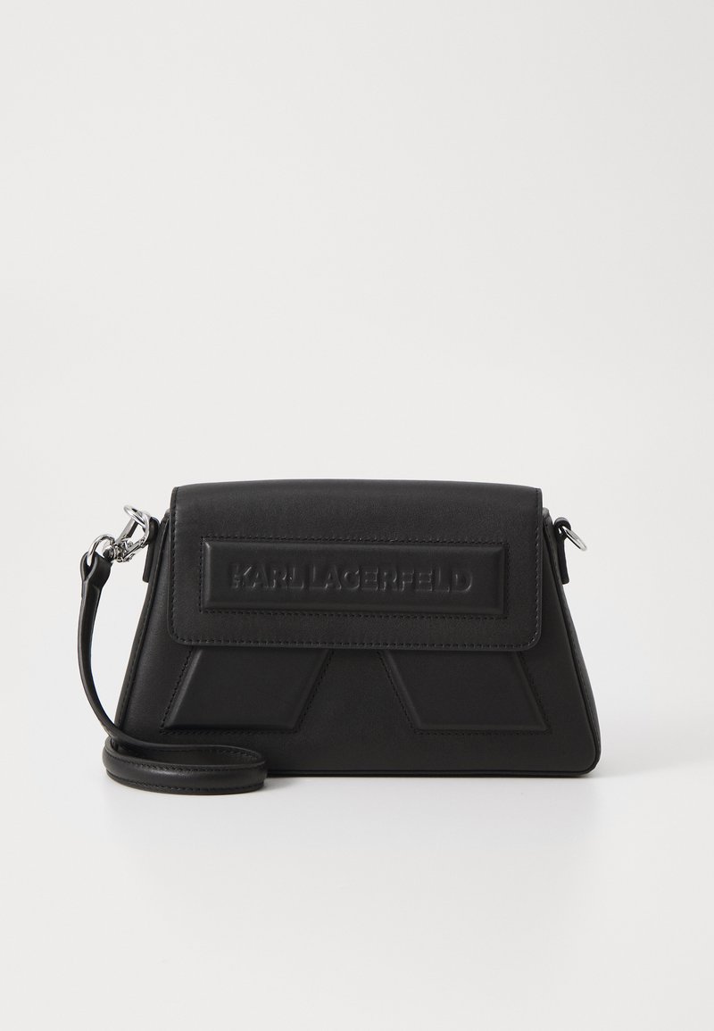 Černá kožená crossbody taška s geometrickým designem, obsahující klopu a embosované logo. Nastavitelný popruh a hladký povrch.