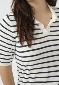 Koszulka polo w kolorze kremowym z granatowymi poziomymi paskami; posiada kołnierzyk i krótkie rękawy; miękki, teksturowany materiał.