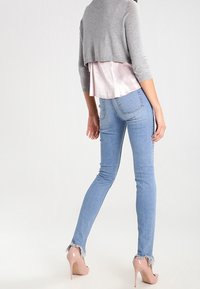 Avskuren grå tröja över en ljusrosa blus, ihop med ljusblå skinny jeans med fransade fållar och nakna högklackade skor.