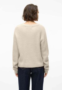 Maglione beige a maglia con una vestibilità comoda, scollatura rotonda e maniche lunghe, abbinato a jeans scuri, che mette in mostra un tessuto testurizzato.
