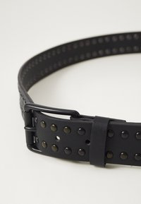 Ceinture en cuir noir dotée de clous métalliques espacés uniformément, avec une finition mate élégante et un design de boucle noire simple. Texturée pour une prise en main et une durabilité.