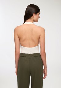 Vista posteriore di un body bianco con scollo a halter abbinato a pantaloni larghi a vita alta verde oliva, con una consistenza liscia e vita elastica.