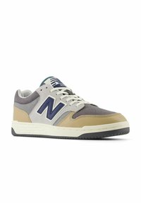 Grijze en tan sneakers met een bovenwerk van leer en suède, voorzien van een marineblauwe "N" logo, witte veters en een gestructureerde rubberen zool.