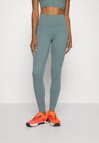 Jasnoniebieskie legginsy bezszwowe z wysokim stanem, w połączeniu z jasnopomarańczowymi butami sportowymi z czarnymi akcentami i fakturowanymi detalami.