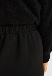 Cintura elástica negra con textura fruncida, combinada con un tejido negro suave y peludo de una prenda, centrándose en los detalles de la costura.