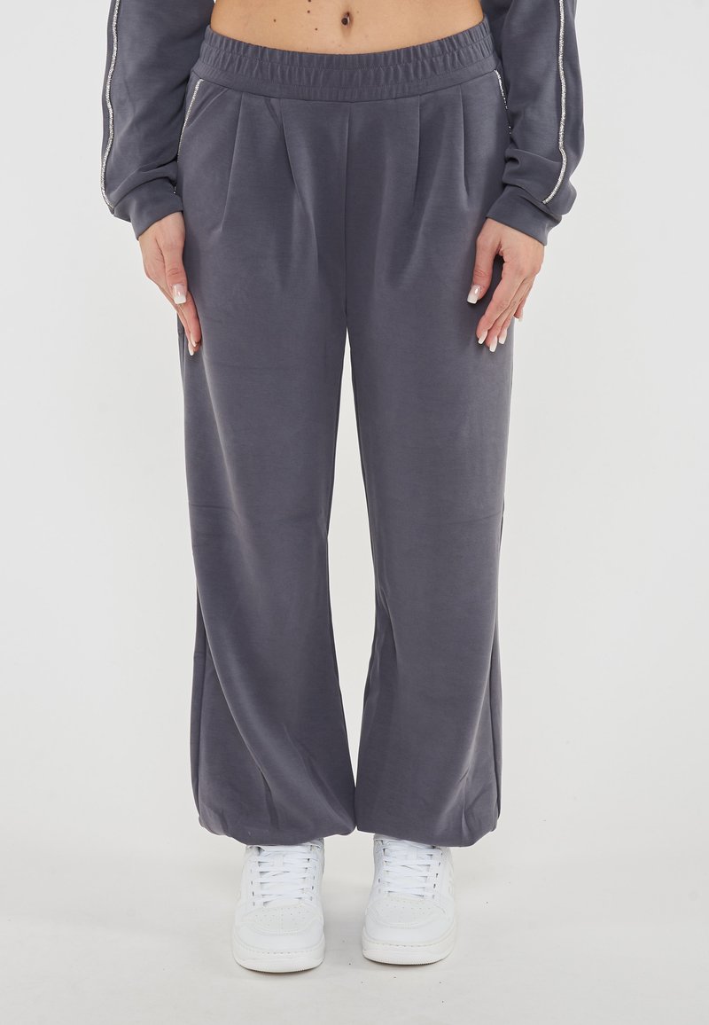 Pantaloni della tuta grigi a vita alta con pieghe e cintura elastica. Tessuto morbido e liscio abbinato a sneaker bianche.