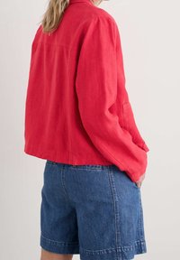 Red linen jacket with a relaxed fit and long sleeves, paired with blue denim shorts featuring side pockets and a casual design.