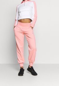 Vaaleanpunainen lyhyt huppari, jossa on valkoisia yksityiskohtia ja etutasku, yhdistettynä vastaaviin vaaleanpunaisiin collegehousuihin. Sisältää joustavat hihansuut ja rentoa muotoilua.