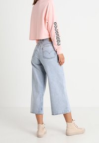 Ljusrosa croppad sweatshirt med "converse" tryckt på ärmen, kombinerad med högmidjade ljusblå denim culotter och beige sneakers.