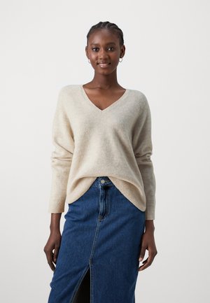 Beige V-hals sweater med lange ærmer, lavet af blødt materiale, sammen med en mørk denimnederdel med en frontslids og en knaplukning.