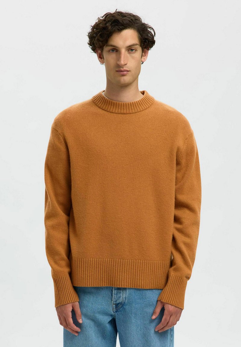Maglione arancione lavorato a maglia con collo rotondo a coste, maniche lunghe e tessuto texturizzato. Indossato con jeans di denim blu chiaro.