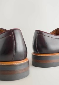 Pantofi din piele de un burgund închis, cu o textură netedă, având un spate rotunjit, o intermediară de culoare maro contrastantă și o talpă subțire de culoare neagră.