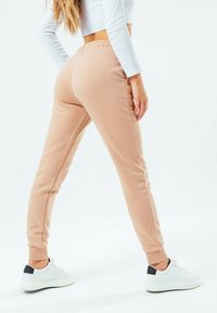 Beige tepláky s přiléhavým střihem, elastickým pasem a žebrovanými manžetami. Spárovány s bílými teniskami s černým akcentem.