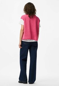 Fuzzy rosa ärmlös topp i lager över en vit T-shirt, parat med vida m�örka denimjeans. Enkelt design utan synliga mönster eller detaljer.