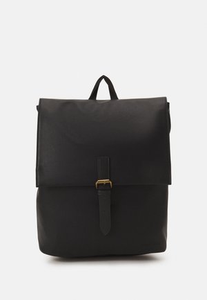 Mochila negra con una textura lisa, que cuenta con una solapa frontal, una correa ajustable con hebilla de latón y un asa superior para llevar.